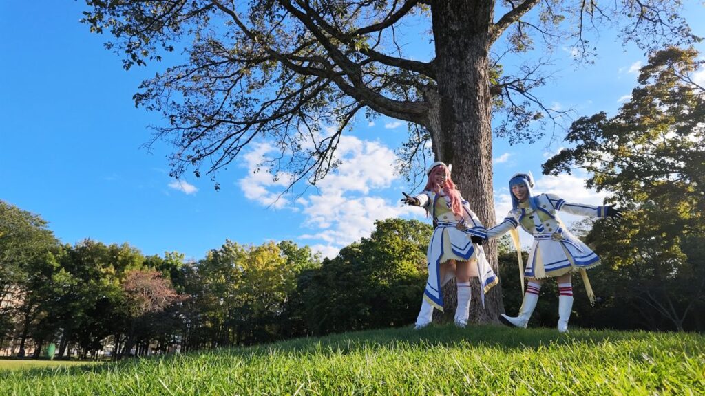 大きな木の下の芝生でポーズをとるコスプレイヤー2人